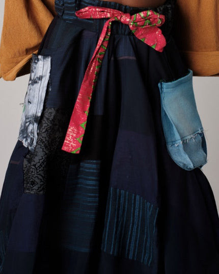 Navy blue skirt with colorful patches and a red ribbon, worn over a mustard yellow cardigan.