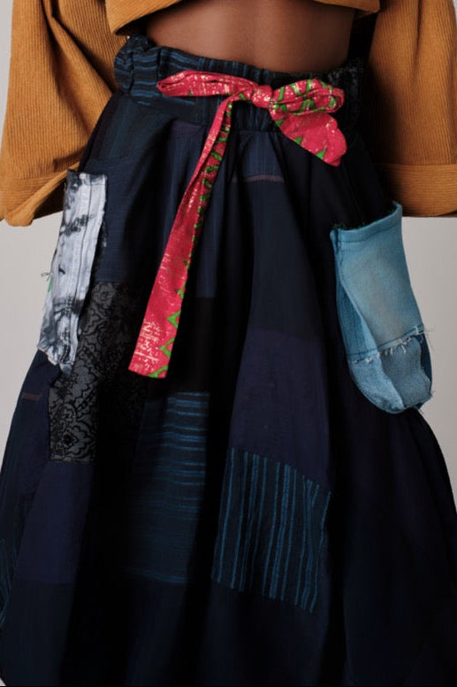 Navy blue skirt with colorful patches and a red ribbon, worn over a mustard yellow cardigan.