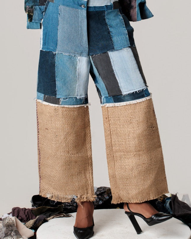 Person wearing a patchwork outfit with blue and brown pants on a white platform.