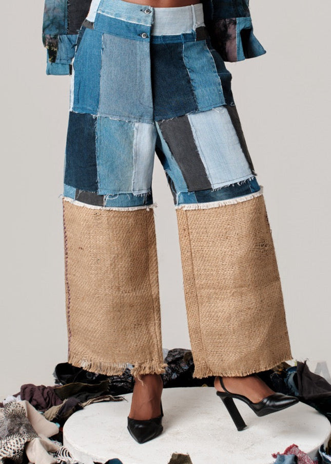 Person wearing a patchwork outfit with blue and brown pants on a white platform.