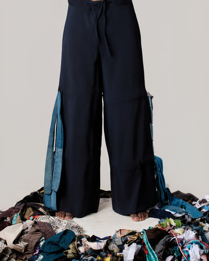 Person wearing dark blue wide-leg pants standing on a pile of clothes against a plain background