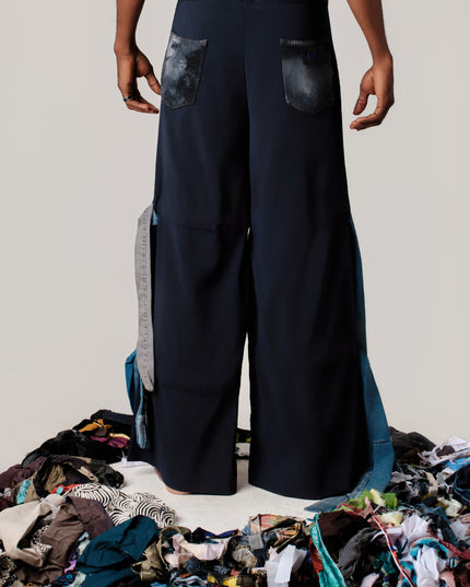 Person wearing wide-leg pants standing over a pile of clothes on a plain background