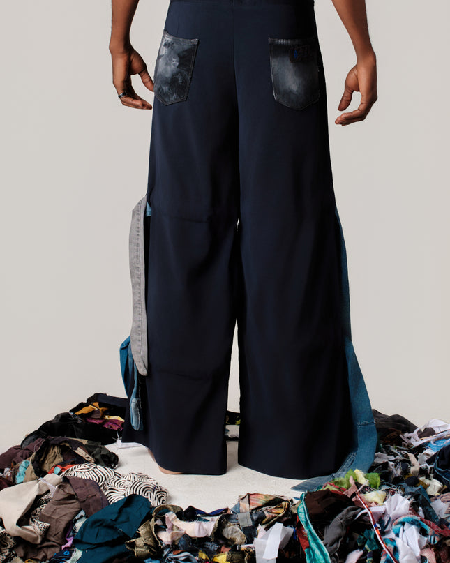 Person wearing wide-leg pants standing over a pile of clothes on a plain background